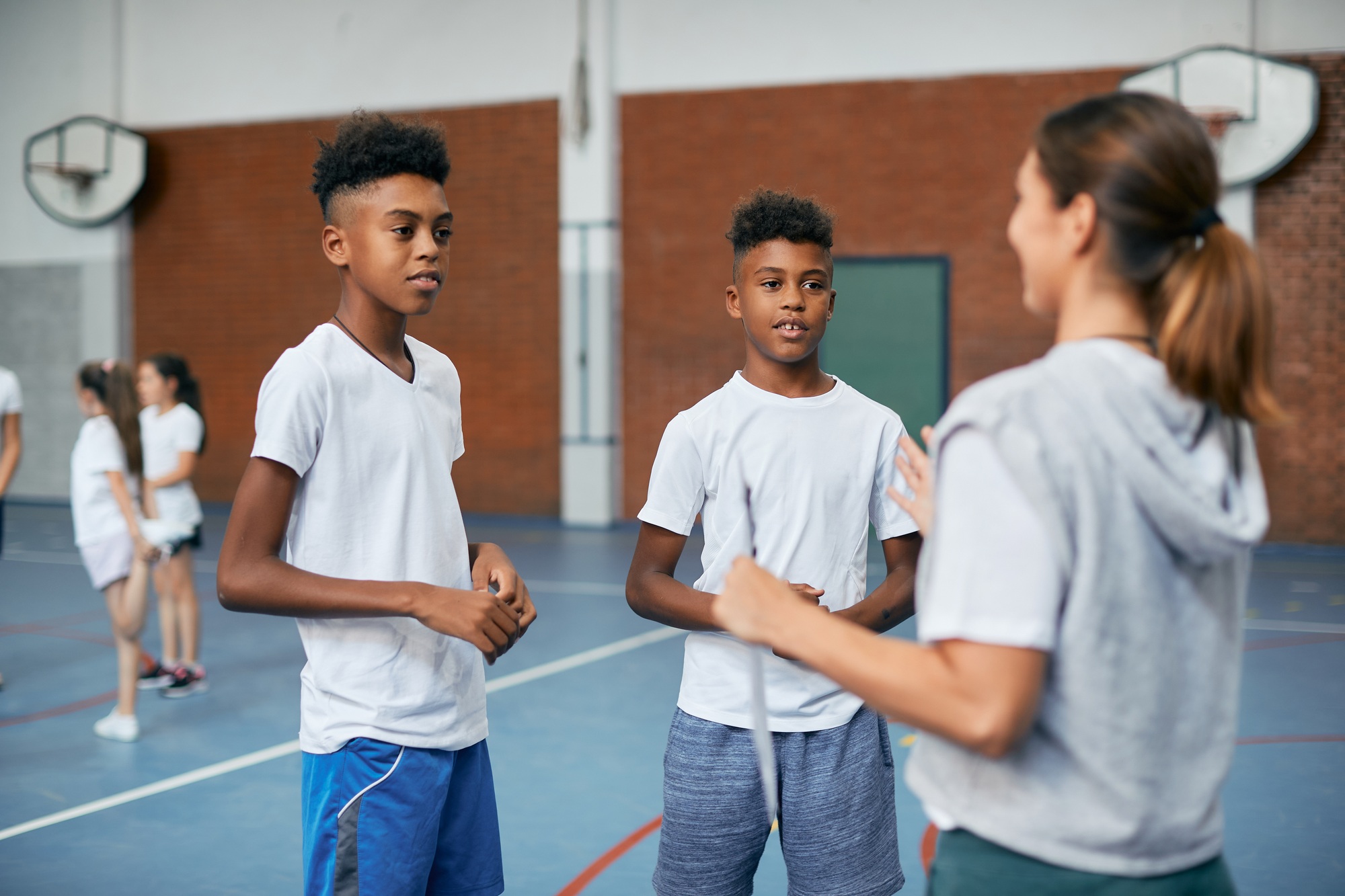 Black elementary students talking to their coach during PE class at school gym.