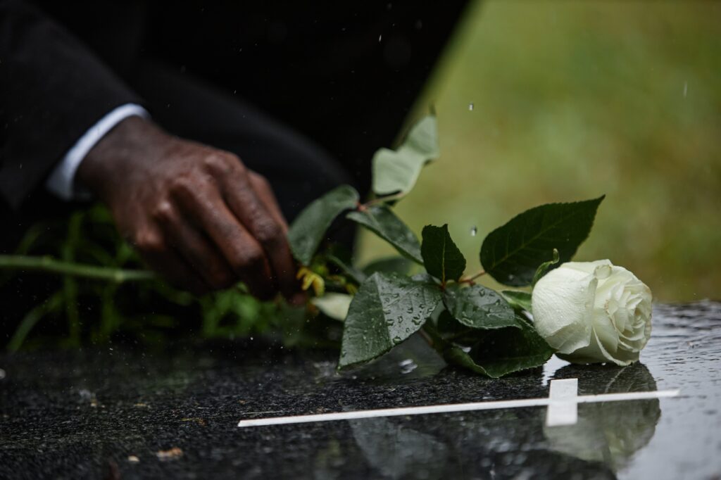 Hand of Black Man Laying Rose on Tombstone during Rain at Graveyard
